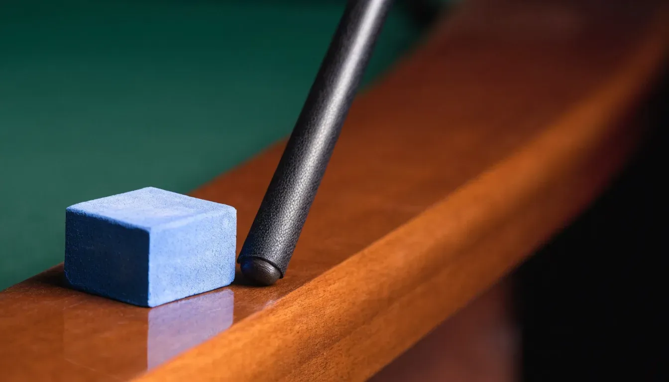 Ein blauer Kreidewürfel und eine Queuespitze liegen am Rand eines Holztischs im weichen Seitenlicht.